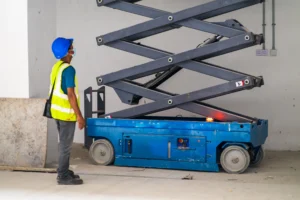 A worker standing beside an extended scissor lift wearing work equipment which could protect him from severe injuries