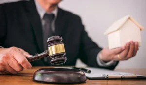 A personal injury claims against landlords solicitor sat at a desk with a gavel in one hand and a small model house in the other.