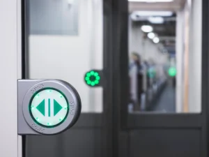 A green buttons with arrows on a door between train carriages which the rail company must keep safe for use