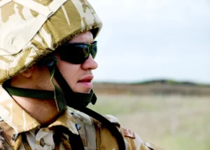 A man in military uniform and wrap around sunglasses/goggles standing on a field.