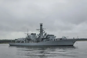 A grey war ship in a harbour on a cloudy day.