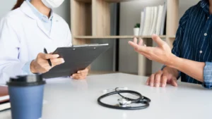 A GP is taking patient notes on a clipboard whilst talking to their patient